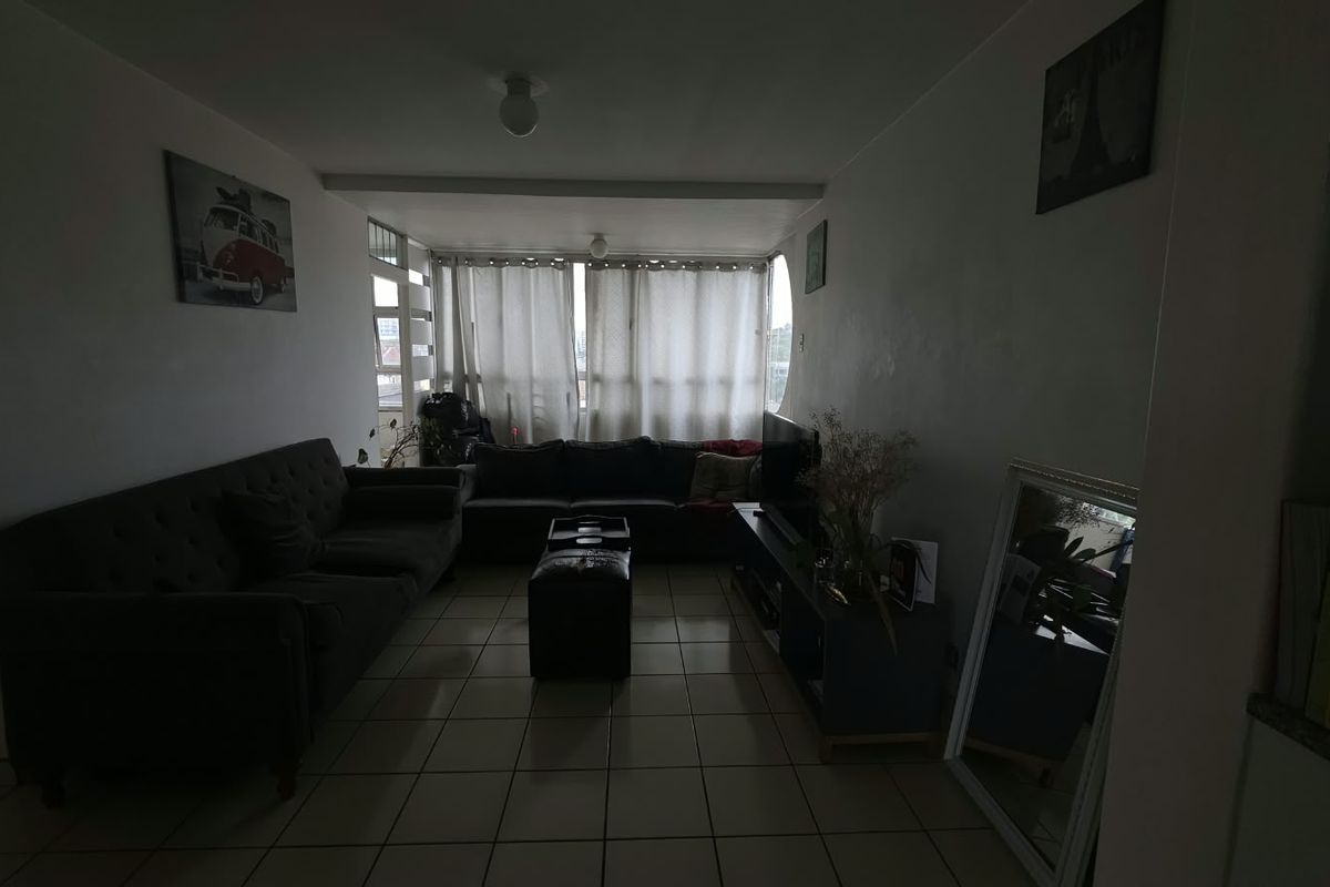 A living room area featuring tiled flooring and a large window, providing natural light to the space.