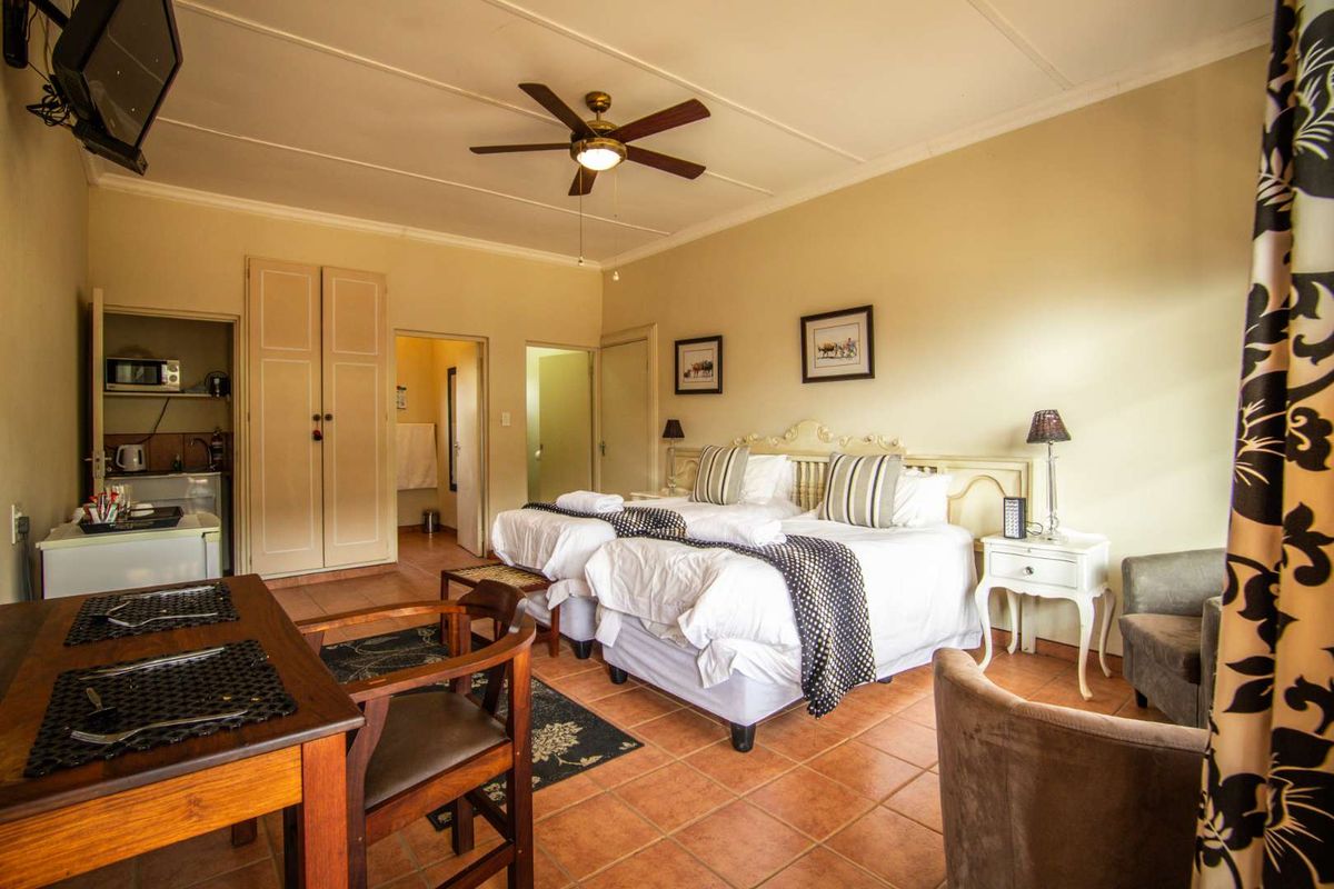 A spacious bedroom featuring tiled flooring, a ceiling fan, and built-in wardrobe storage, with direct access to an en-suite bathroom.