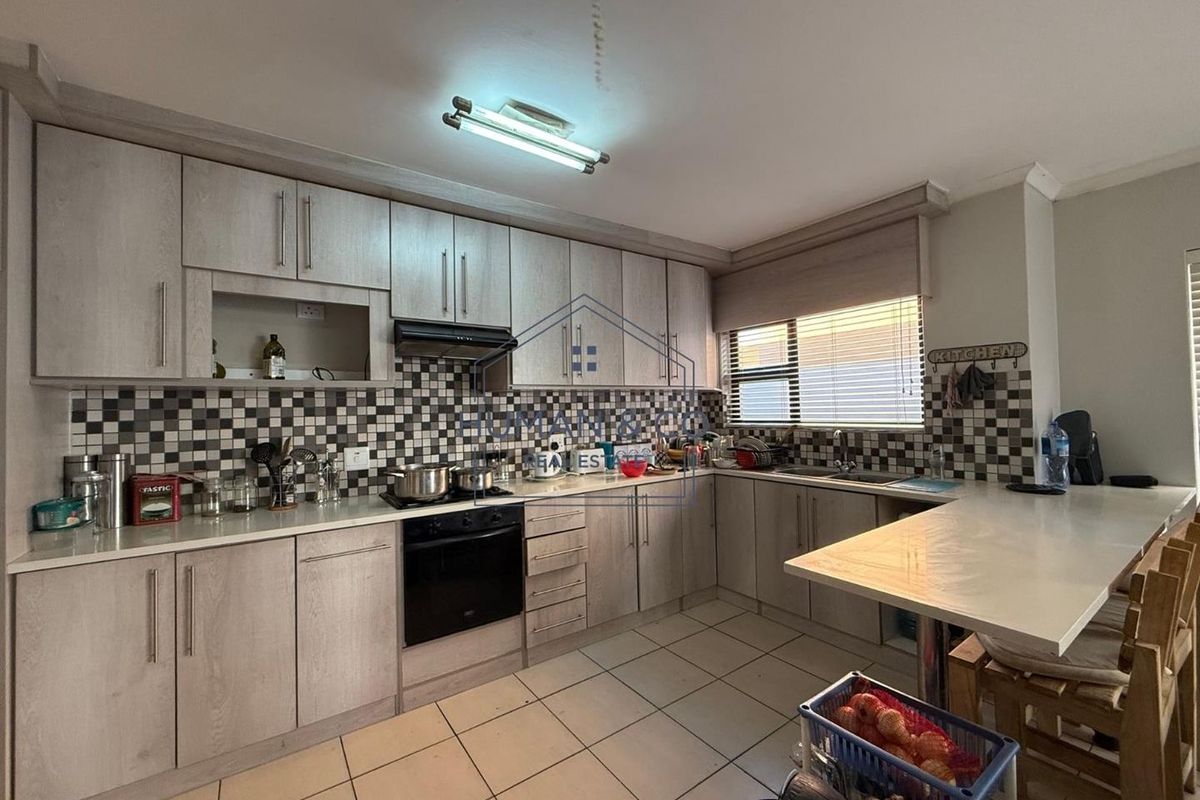 Functional kitchen featuring light wood-grain cabinetry, integrated oven, extractor fan, and a breakfast bar counter with tiled flooring.