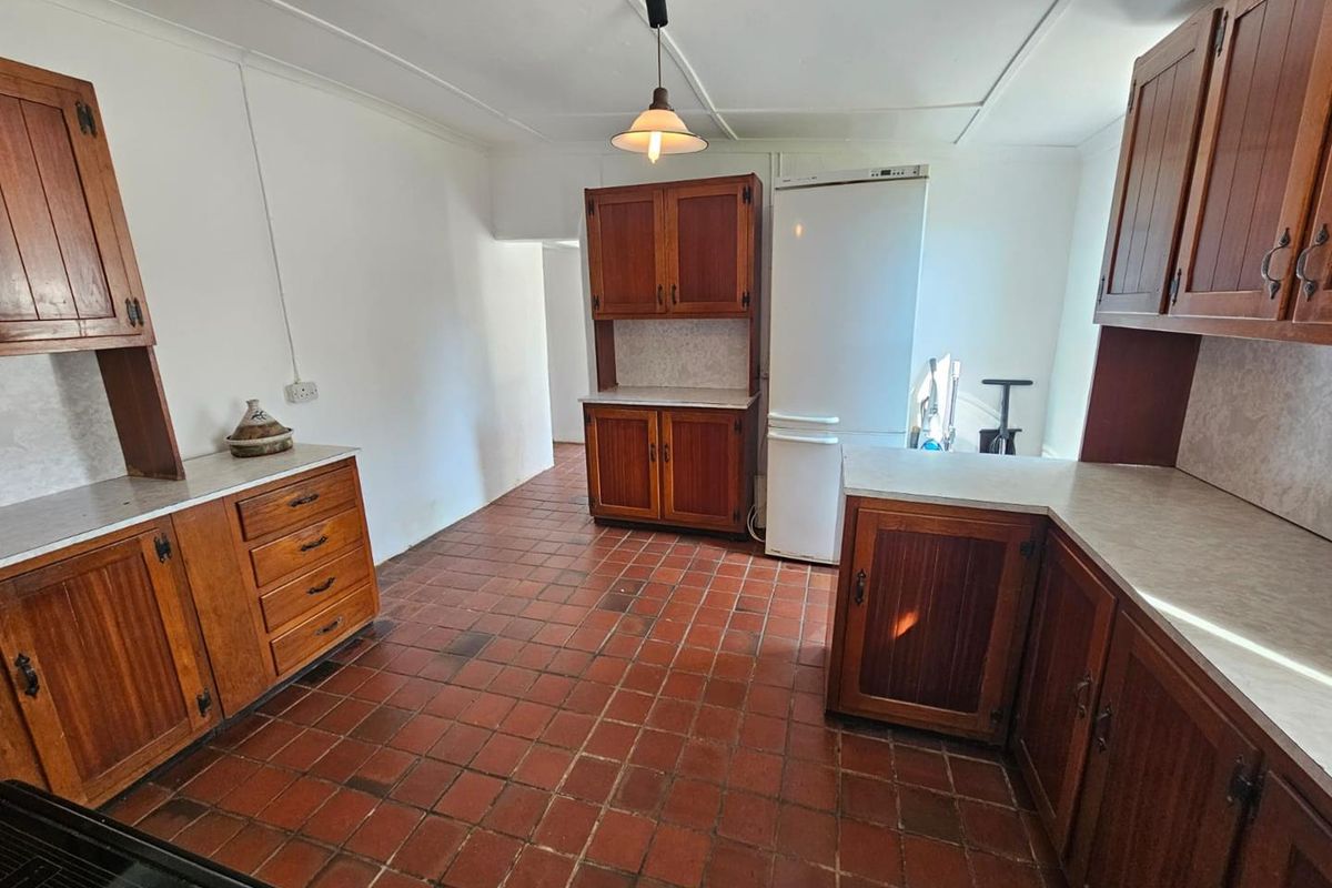 A functional kitchen featuring traditional wooden cabinetry, laminate countertops, and durable terracotta-style floor tiles, offering a classic farmhouse aesthetic.