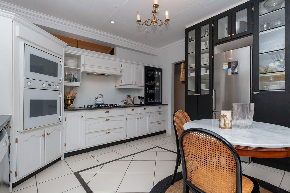 A well-appointed kitchen featuring contrasting black and white cabinetry, built-in double ovens, a gas hob, and tiled flooring with decorative inlay.