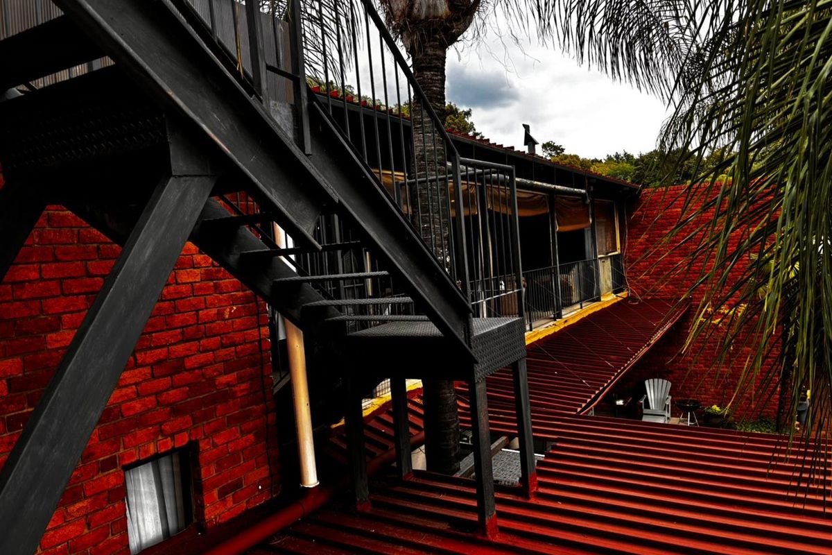 Exterior view of a commercial property featuring a red brick facade, corrugated metal roofing, and an external black metal staircase leading to an upper level.