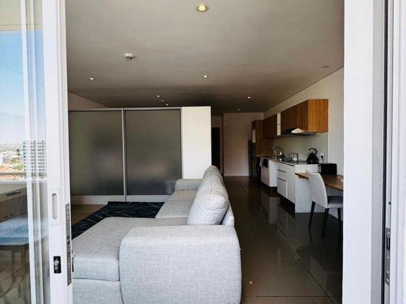 Modern open-plan apartment featuring a sleek kitchen with built-in cabinetry and tiled flooring, seamlessly flowing into the living area with balcony access.