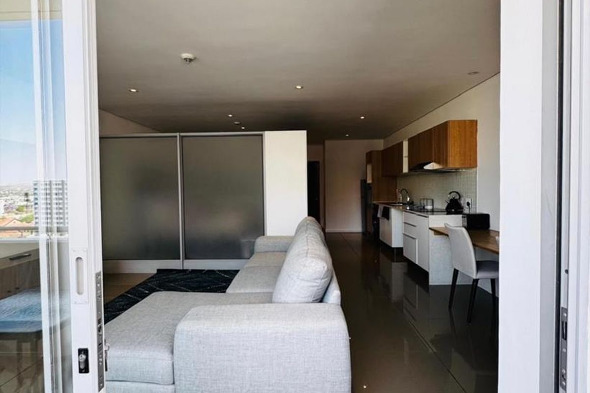 Modern open-plan apartment featuring a sleek kitchen with built-in cabinetry and tiled flooring, seamlessly flowing into the living area with balcony access.