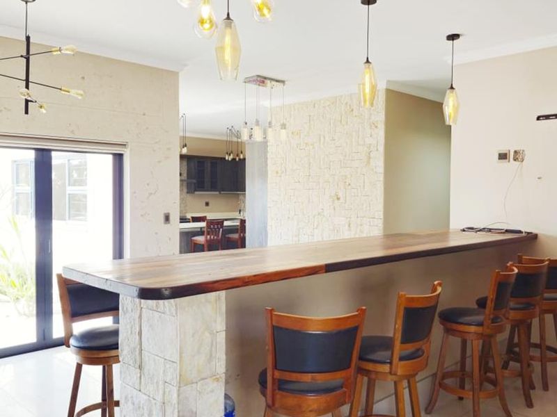 Spacious open-plan living area featuring a stone-clad breakfast bar with timber countertop, tiled flooring, and modern pendant lighting, leading to a kitchen area.