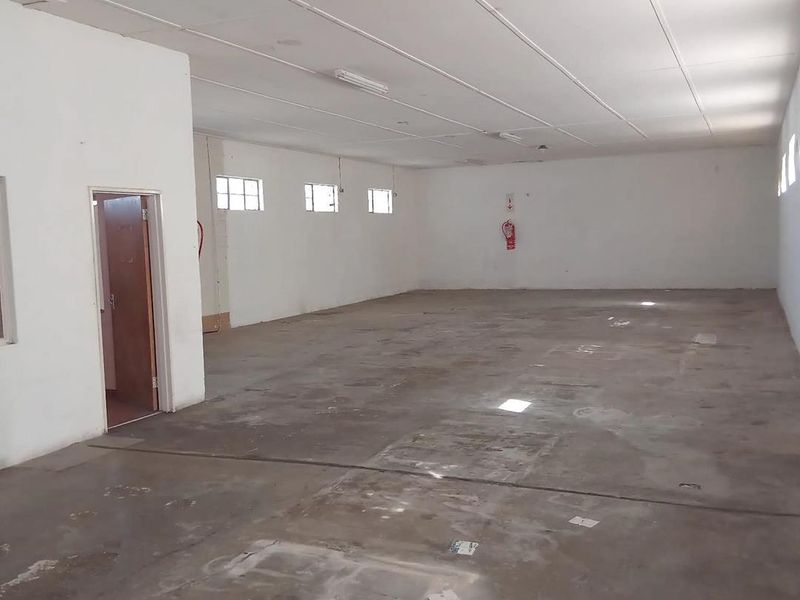 A spacious, empty industrial utility area featuring concrete flooring, a suspended ceiling, and basic fluorescent lighting, suitable for storage or workshop use.