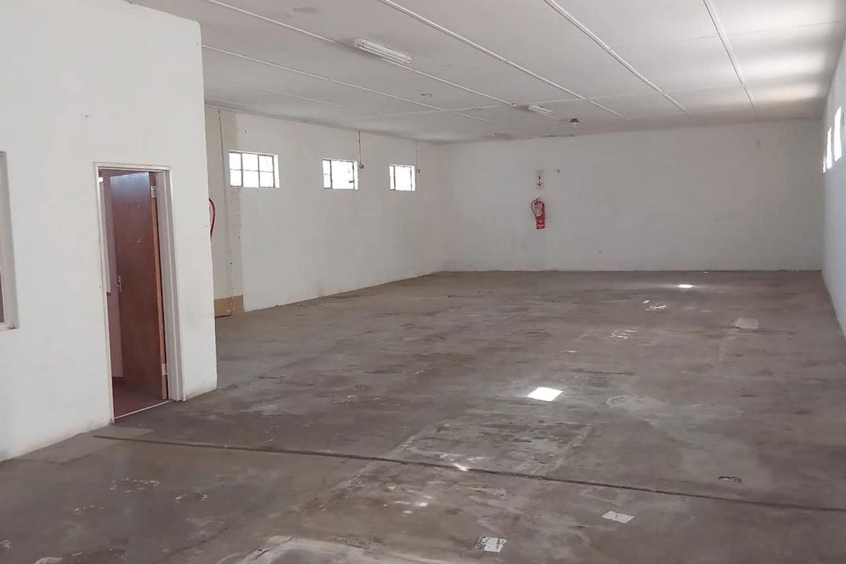 A spacious, empty industrial utility area featuring concrete flooring, a suspended ceiling, and basic fluorescent lighting, suitable for storage or workshop use.