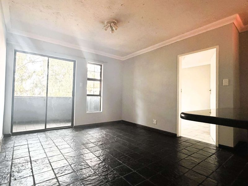 An empty living area featuring dark tiled flooring, a breakfast bar, and a sliding glass door leading to an outdoor space.