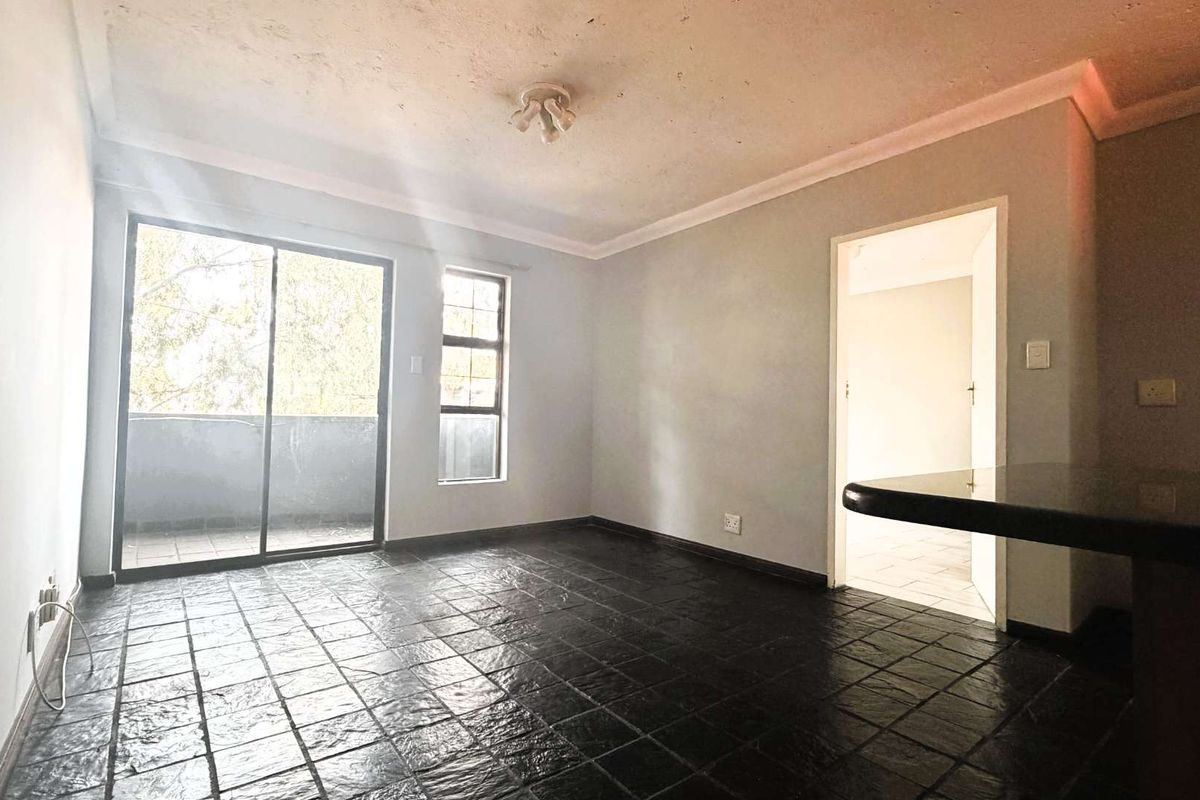 An empty living area featuring dark tiled flooring, a breakfast bar, and a sliding glass door leading to an outdoor space.