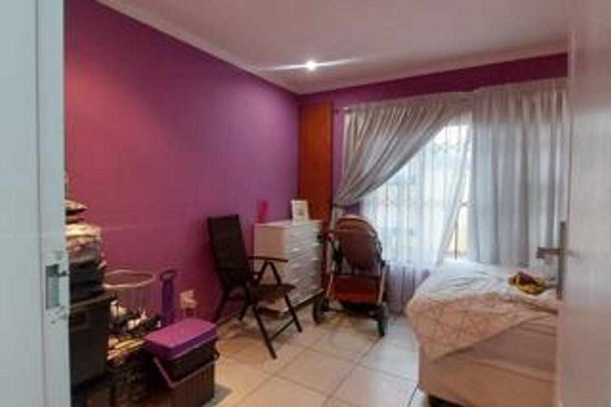 A bedroom featuring tiled flooring and a large window with security bars, finished with a bold purple accent wall.