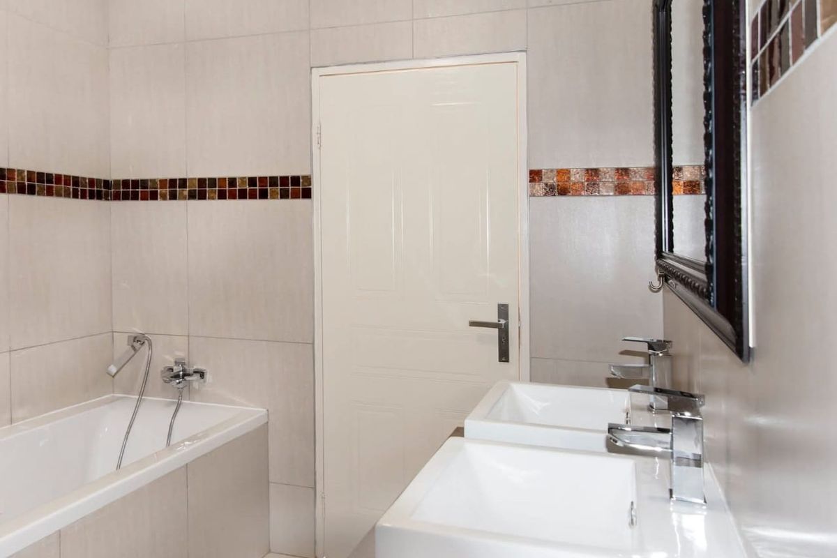 A modern bathroom featuring a built-in bathtub, double vanity with chrome faucets, and decorative mosaic tile accents.