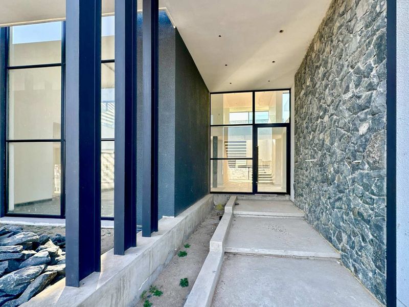 Modern architectural entrance featuring stone cladding, steel structural columns, and expansive glass windows leading into a bright, contemporary interior space.