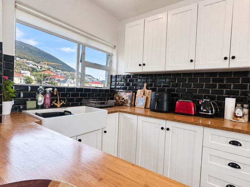 A well-maintained kitchen featuring white shaker cabinetry, wooden countertops, a classic farmhouse sink, and a striking black subway tile backsplash with mountain views.