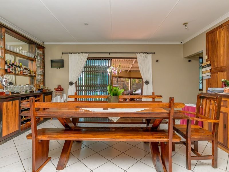Dining room featuring built-in wooden bar cabinetry, glass shelving, tiled flooring, and sliding glass doors leading to an outdoor area.