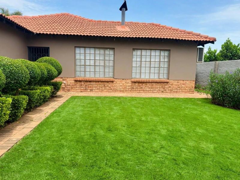 A well-maintained rear exterior view of the house featuring a manicured lawn, paved walkway, and classic brick and tile facade.
