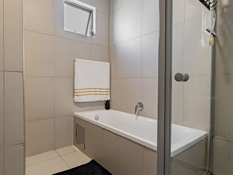 A modern bathroom featuring a built-in bathtub, a glass-enclosed shower, and neutral floor-to-ceiling wall tiles.
