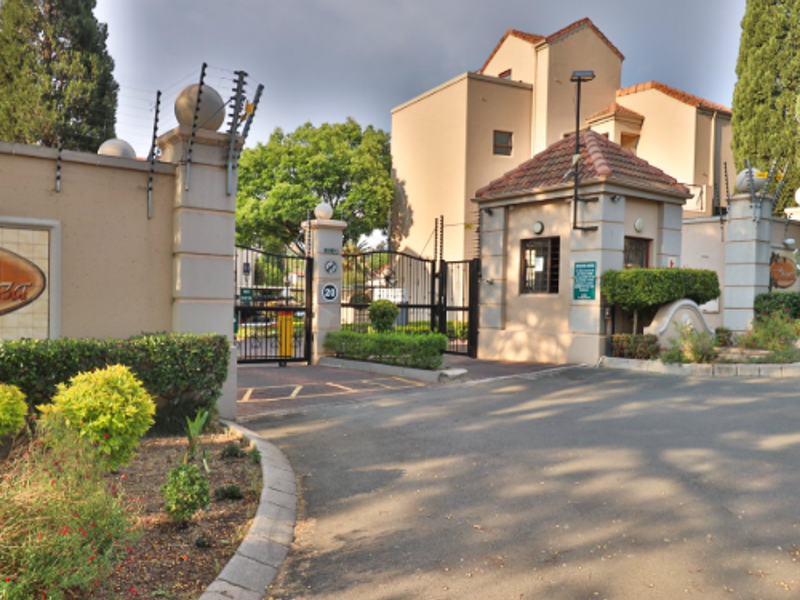 The entrance to the apartment complex features a secure gated access point with a guard house, perimeter wall, and electric fencing.