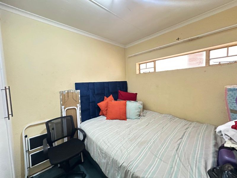 A compact bedroom featuring a built-in cupboard and a high-level horizontal window, requiring cosmetic updates to the wall finishes.