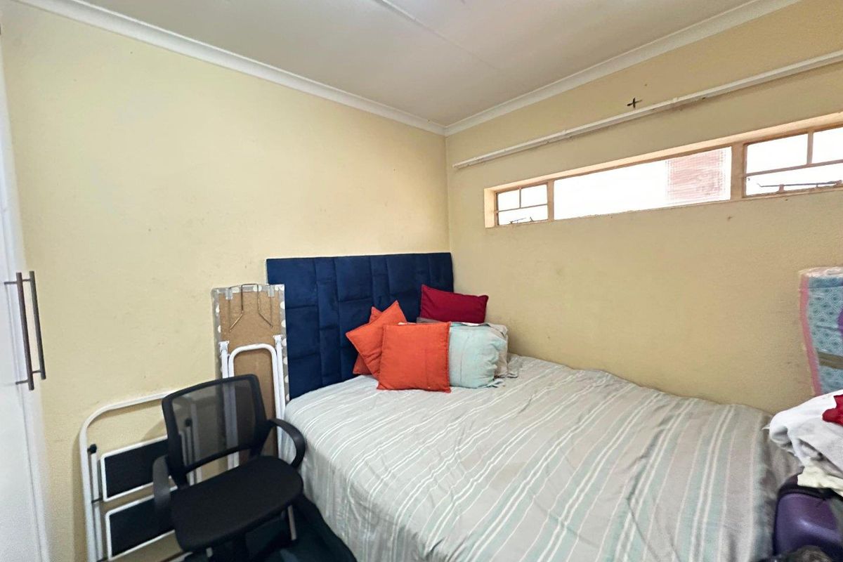 A compact bedroom featuring a built-in cupboard and a high-level horizontal window, requiring cosmetic updates to the wall finishes.