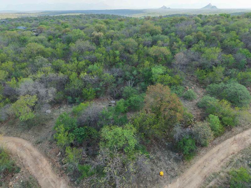 An aerial view of a vacant residential plot featuring natural bushveld vegetation and dirt access roads, set against a scenic landscape backdrop.