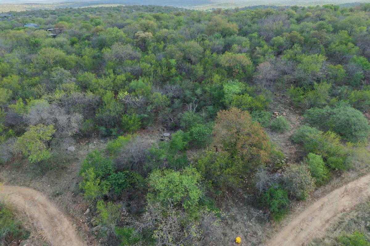 An aerial view of a vacant residential plot featuring natural bushveld vegetation and dirt access roads, set against a scenic landscape backdrop.