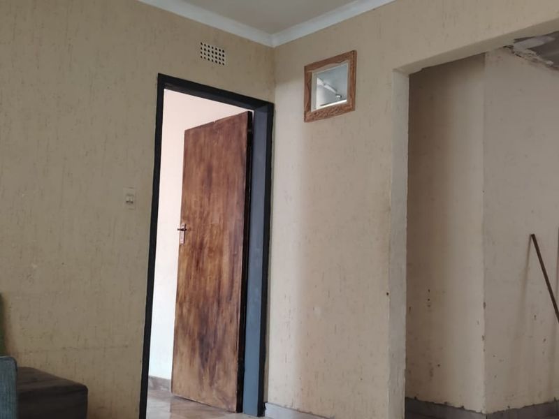 An empty living area featuring tiled flooring, timber doors, and ventilation grilles, requiring cosmetic updates to the wall finishes and ceiling edges.
