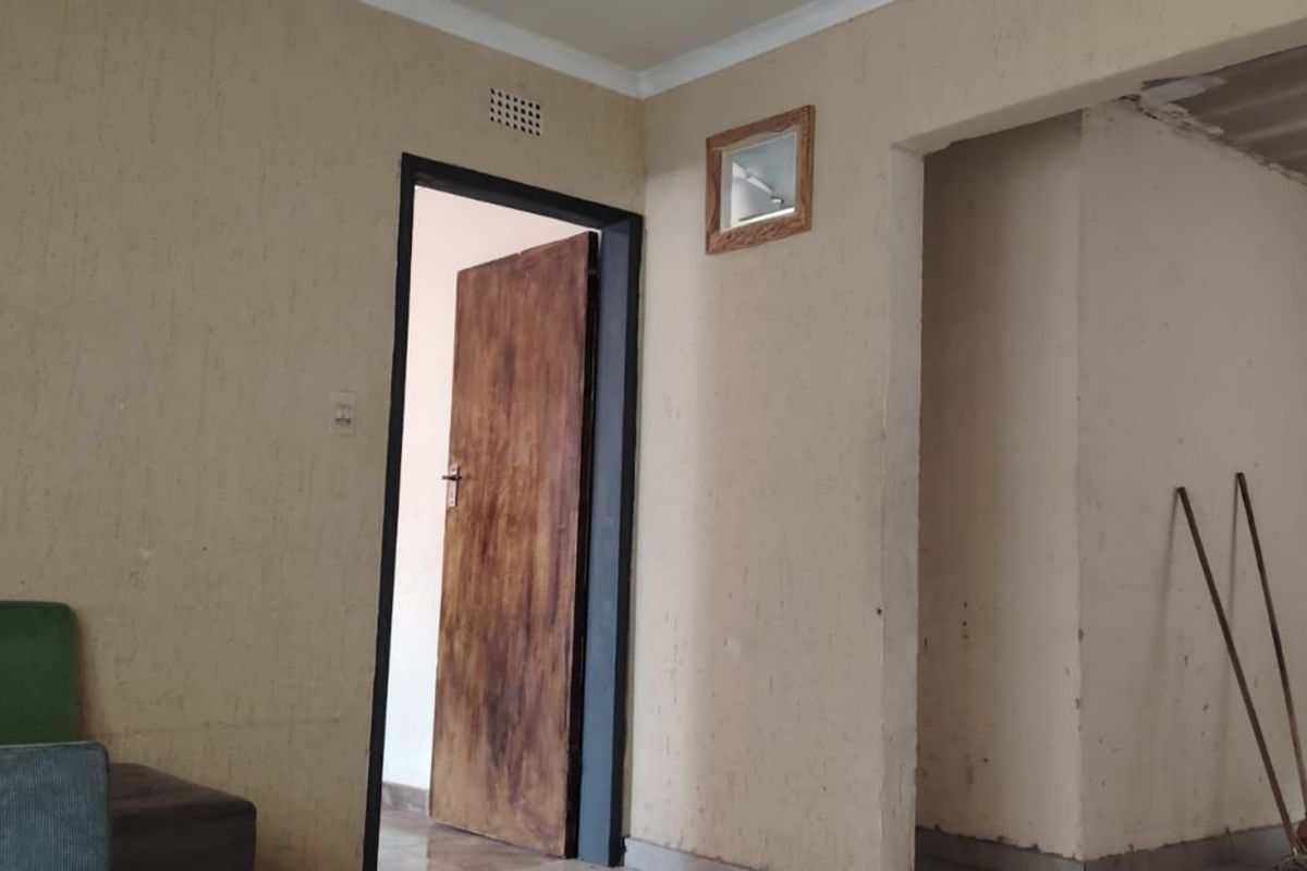 An empty living area featuring tiled flooring, timber doors, and ventilation grilles, requiring cosmetic updates to the wall finishes and ceiling edges.