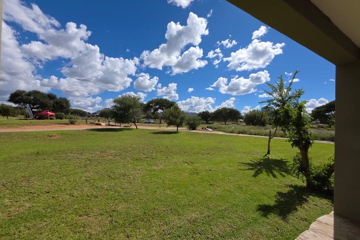 A view from a covered patio overlooking a spacious, well-maintained green lawn and natural landscape under a bright blue sky.