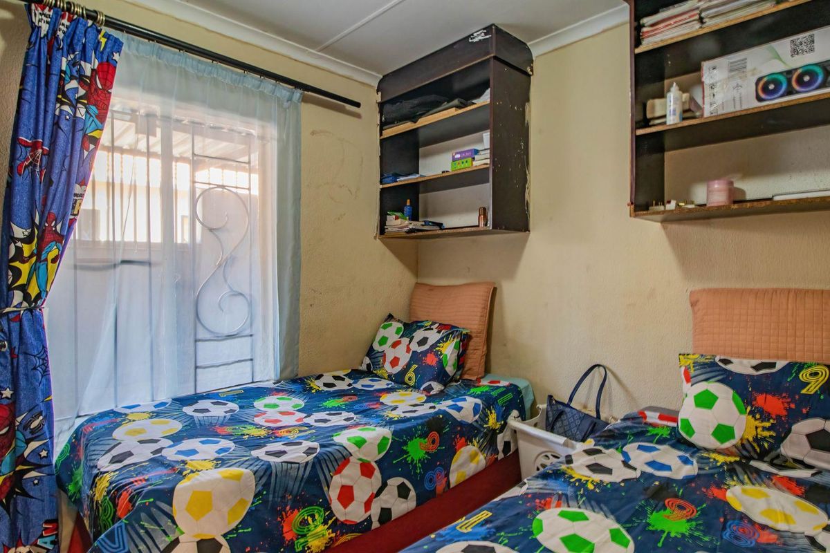 A compact bedroom featuring built-in wall shelving and a security gate on the window, providing functional storage and basic security.