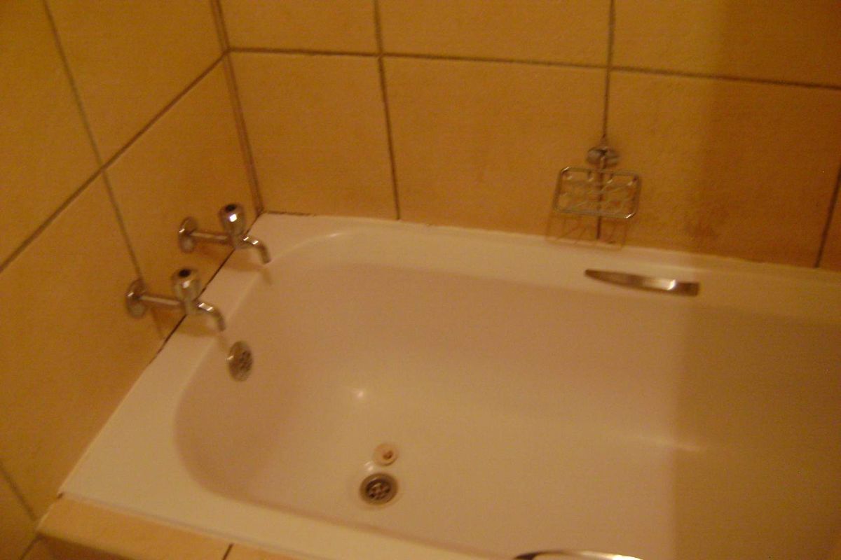A standard bathroom featuring a built-in bathtub with wall-mounted chrome faucets and neutral ceramic wall tiling.