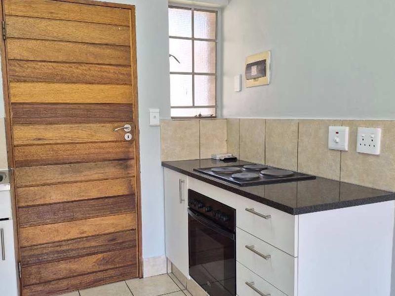 A compact kitchen featuring built-in oven, electric hob, granite countertops, tiled backsplash, and neutral tiled flooring, providing a functional and clean workspace.