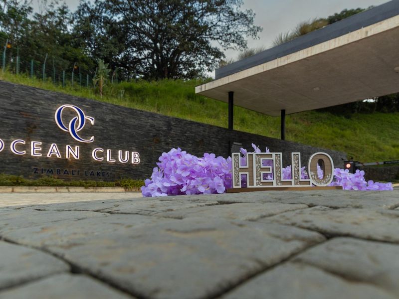 The entrance to Ocean Club at Zimbali Lakes, featuring a modern stone-clad wall with illuminated signage and a paved driveway.