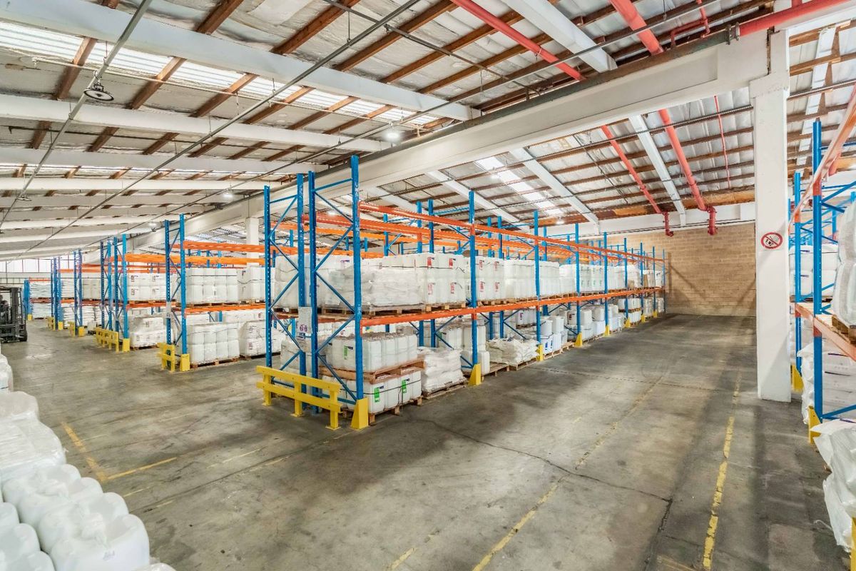 Spacious industrial warehouse featuring high ceilings with exposed steel trusses, fire sprinkler system, concrete flooring, and extensive built-in pallet racking for storage.