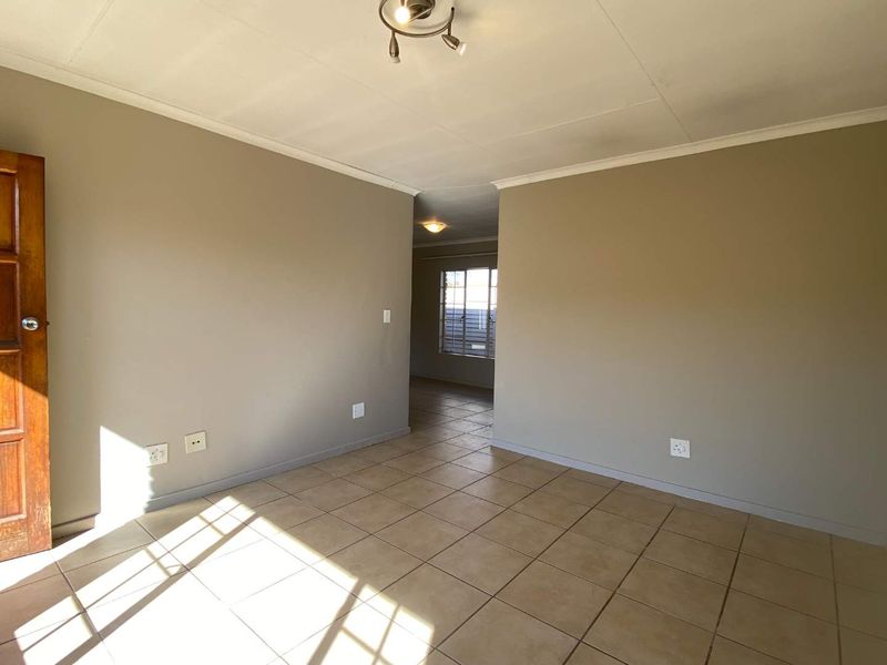 An empty, open-plan living area featuring neutral wall tones, ceramic floor tiles, and a coved ceiling, providing a blank canvas for interior design.