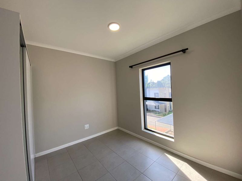 A clean, empty bedroom featuring neutral wall paint, tiled flooring, a built-in wardrobe, and a window with a curtain rod.