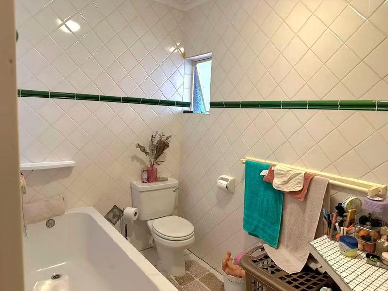 A functional bathroom featuring white wall tiles with a decorative green border, a standard bathtub, and a toilet.