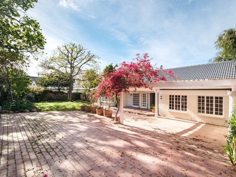A spacious rear exterior featuring a brick-paved patio area, a pergola, and classic french doors leading into the home, set against a landscaped garden.
