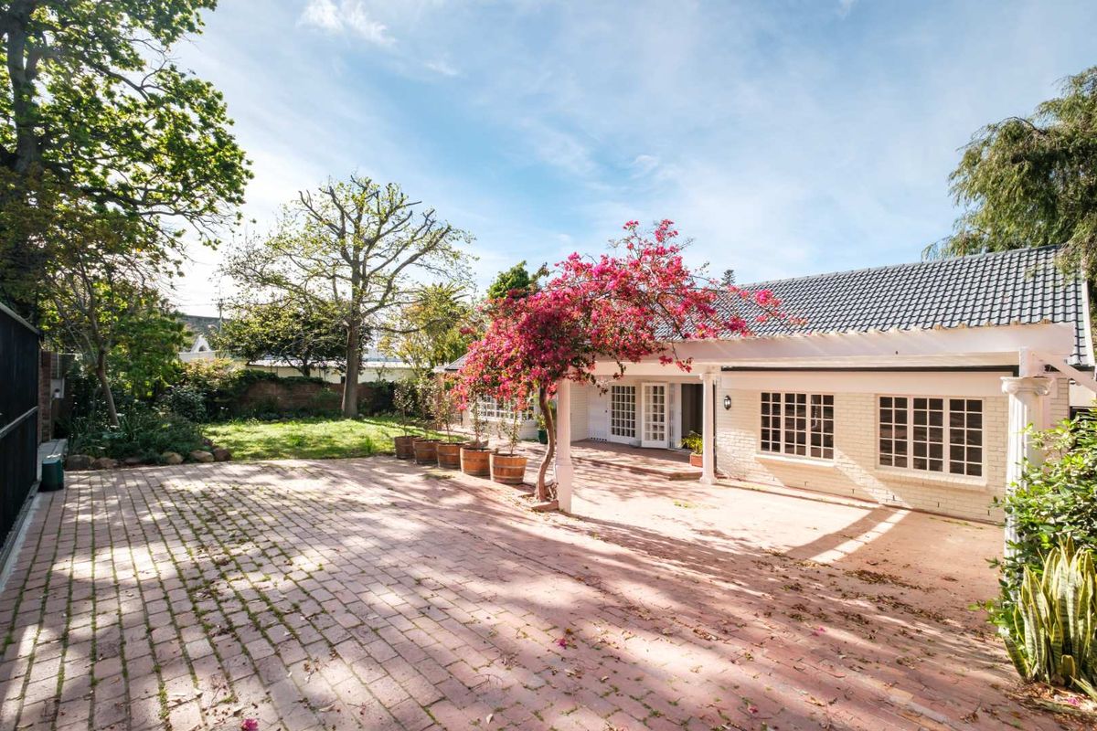 A spacious rear exterior featuring a brick-paved patio area, a pergola, and classic french doors leading into the home, set against a landscaped garden.