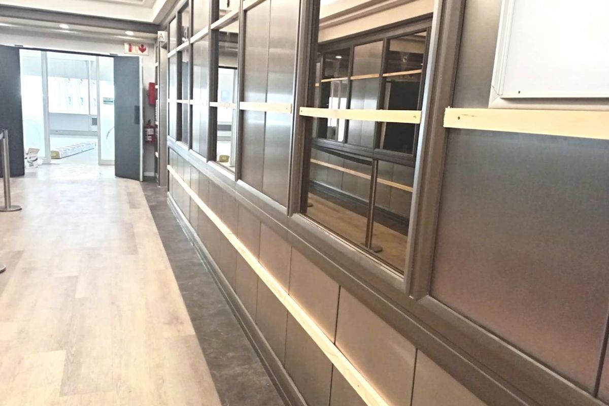 A modern office hallway featuring glass partition walls, wood-look laminate flooring, and recessed ceiling lighting, currently in a clean, vacant state.