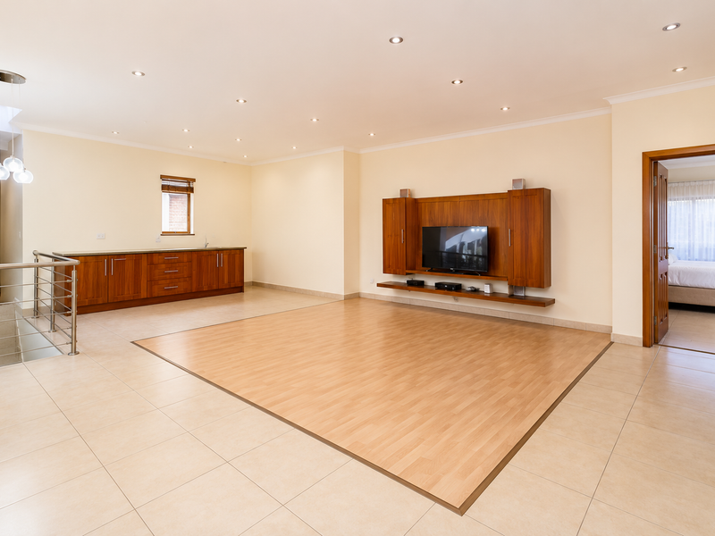 Spacious open-plan living area featuring a combination of tiled and laminate flooring, built-in cabinetry, and a custom media unit.