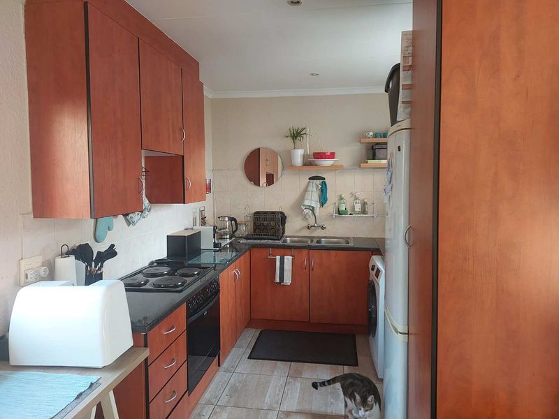 Compact kitchen featuring wooden cabinetry, dark countertops, integrated electric hob and oven, and tiled flooring with a functional layout.