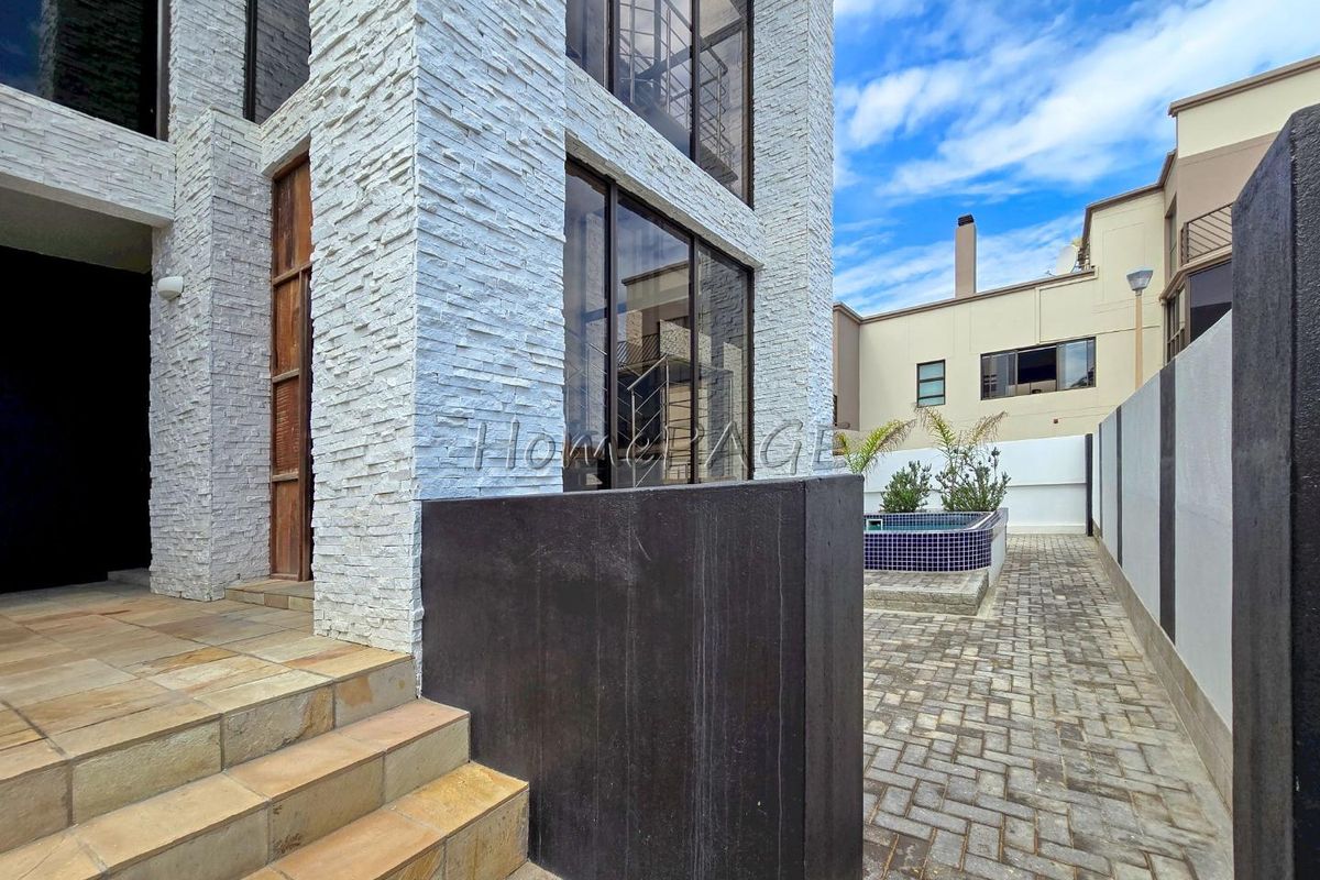 A modern exterior view featuring stacked stone cladding, large glass windows, paved courtyard, and a small tiled plunge pool.