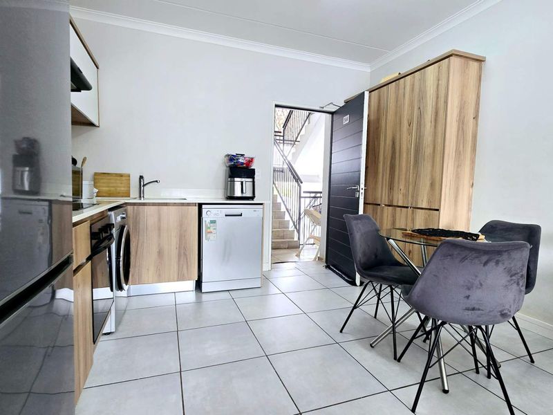 Modern open-plan kitchen and dining area featuring light wood cabinetry, tiled flooring, and direct access to the building entrance.