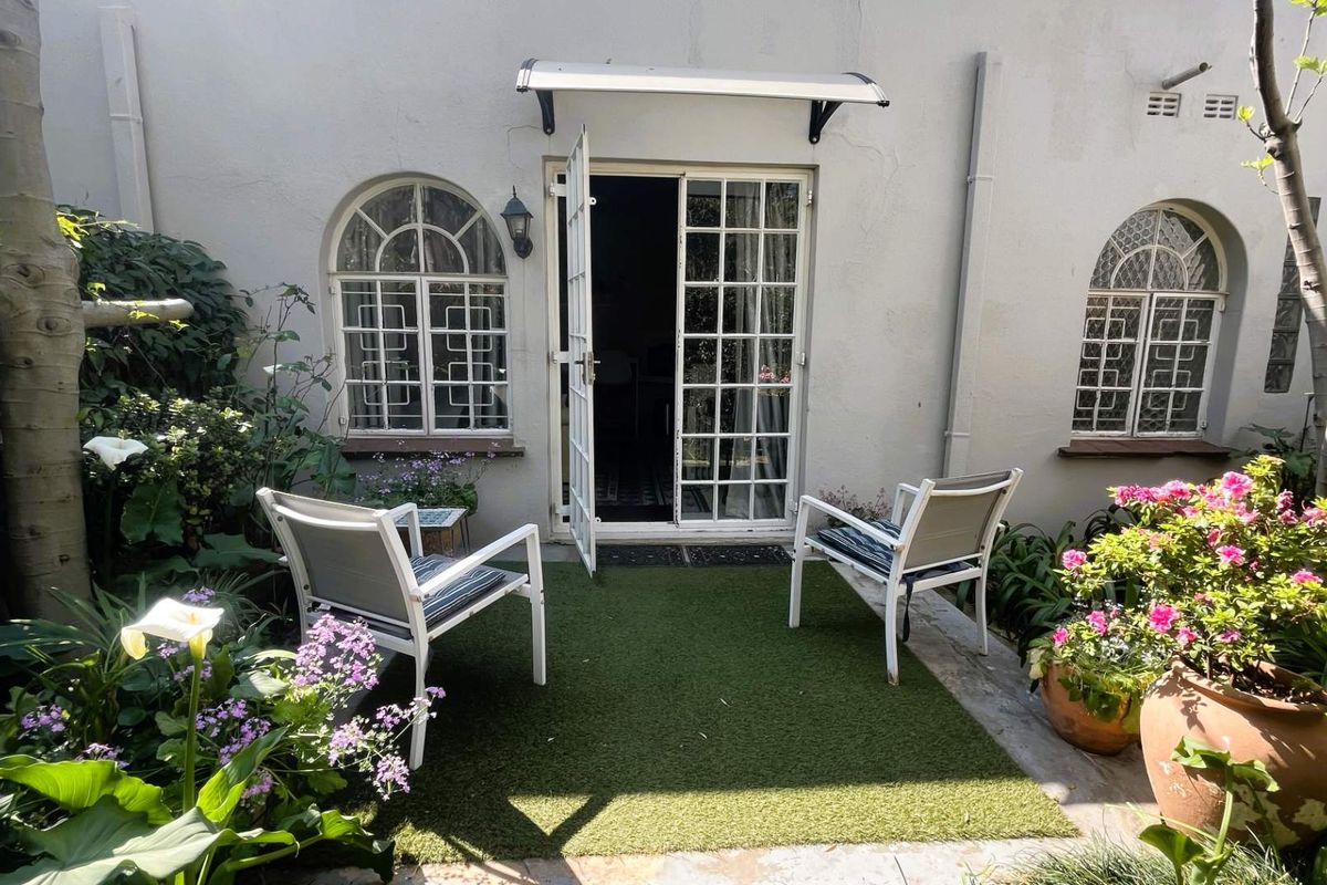 A charming rear courtyard featuring arched windows, classic french doors with an awning, and a well-maintained artificial turf area.