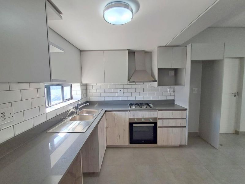 Modern kitchen featuring light wood-tone cabinetry, stone countertops, subway tile backsplash, and integrated stainless steel appliances including a gas hob and oven.