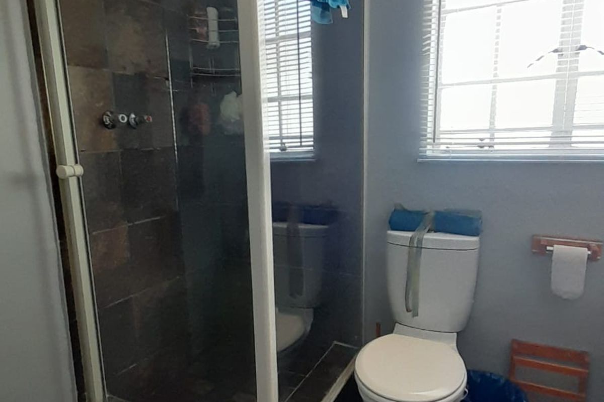 A functional bathroom featuring a tiled shower enclosure, a standard toilet, and tiled flooring with natural light from a window.