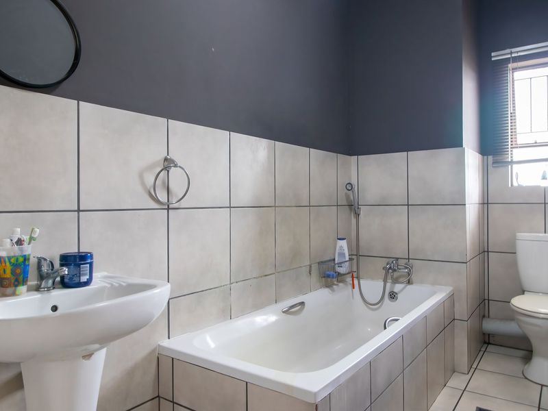 A functional bathroom featuring a pedestal basin, built-in bathtub with handheld shower mixer, and a standard toilet, finished with neutral wall and floor tiling.