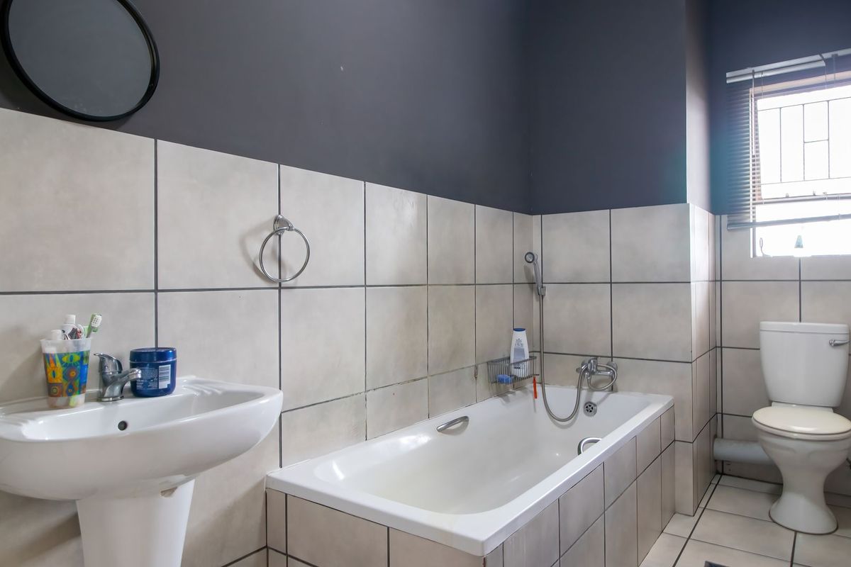 A functional bathroom featuring a pedestal basin, built-in bathtub with handheld shower mixer, and a standard toilet, finished with neutral wall and floor tiling.
