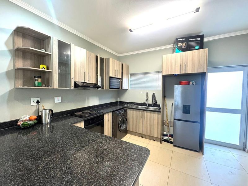 Modern kitchen featuring granite countertops, built-in cabinetry, integrated appliances, and tiled flooring with direct access to an exterior door.