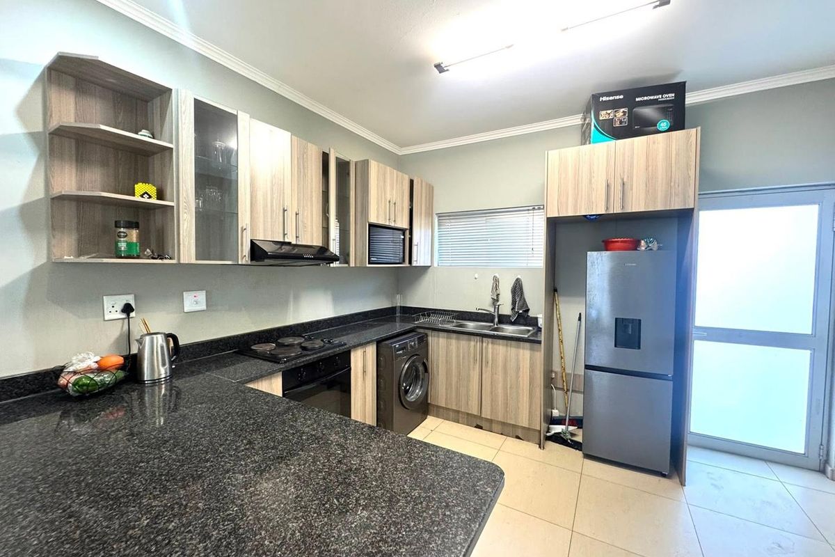 Modern kitchen featuring granite countertops, built-in cabinetry, integrated appliances, and tiled flooring with direct access to an exterior door.